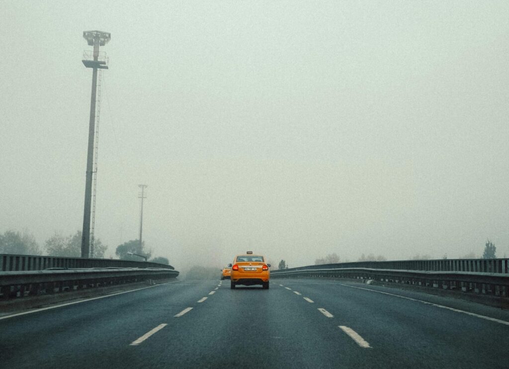 A lone taxi drives down a foggy highway, creating a sense of solitude and mystery.